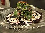 Frisch angerichteter Kräutersalat auf einem kunstvollen Soßenspiegel.