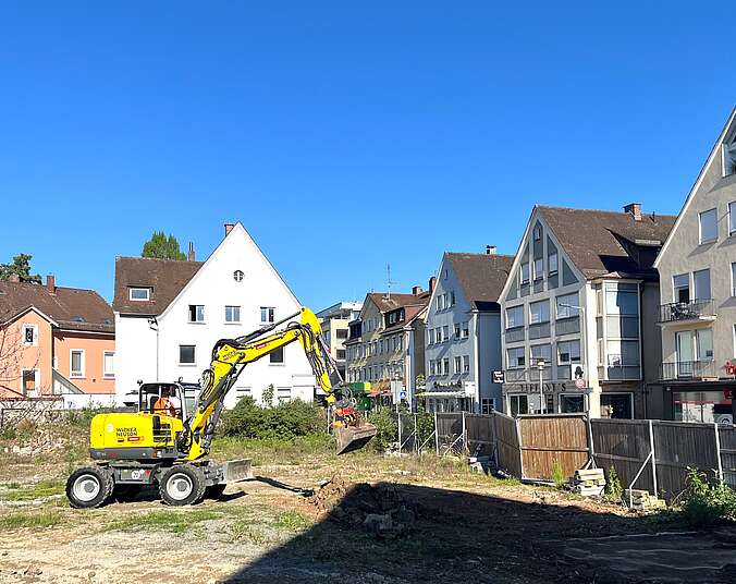 Bagger auf Baustelle, im Hintergrund Häuser