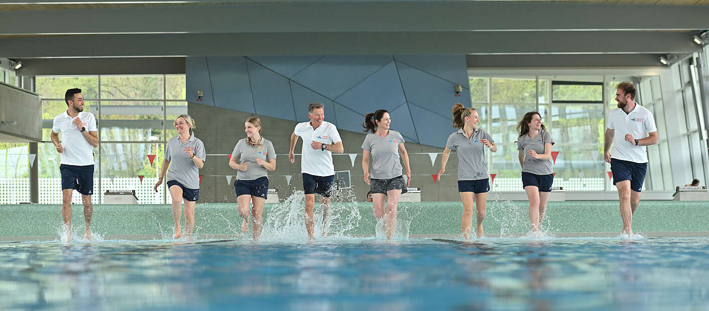 Sportbad-Mitarbeiter rennen hand in hand lachend durch flaches Wasser
