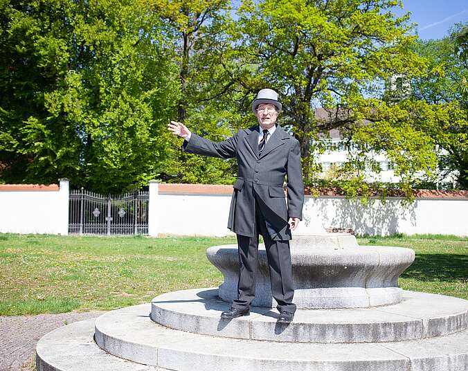 Mann im Gehrock und mit Zylinder steht auf Stufen in einem Park.