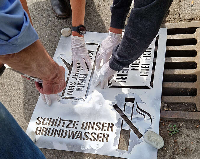 Hände, die auf den Boden mit Sprühflaschen einen Gully beschriften