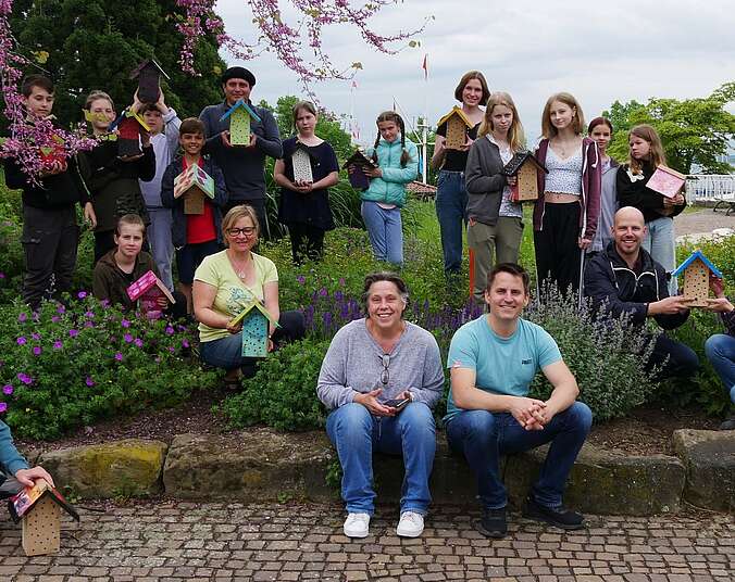 Eine Gruppe von Kindern und Erwachsenen zeigen Insektenhäuschen.