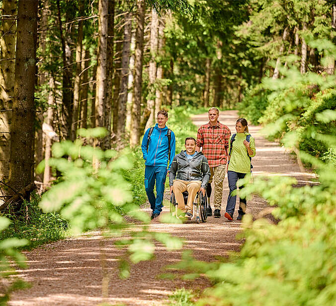 Spaziergänger mit einem Rolstuhlfahrer im Wald