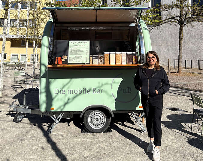 Frau steht vor Foodtruck-Anhänger der Pop-up-Gastronomie PuB – Perspektiven und Begegnungen auf dem Adenauerplatz