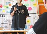 Jugendlicher mit Mikrofon stellt Projekt vor Stellwand vor