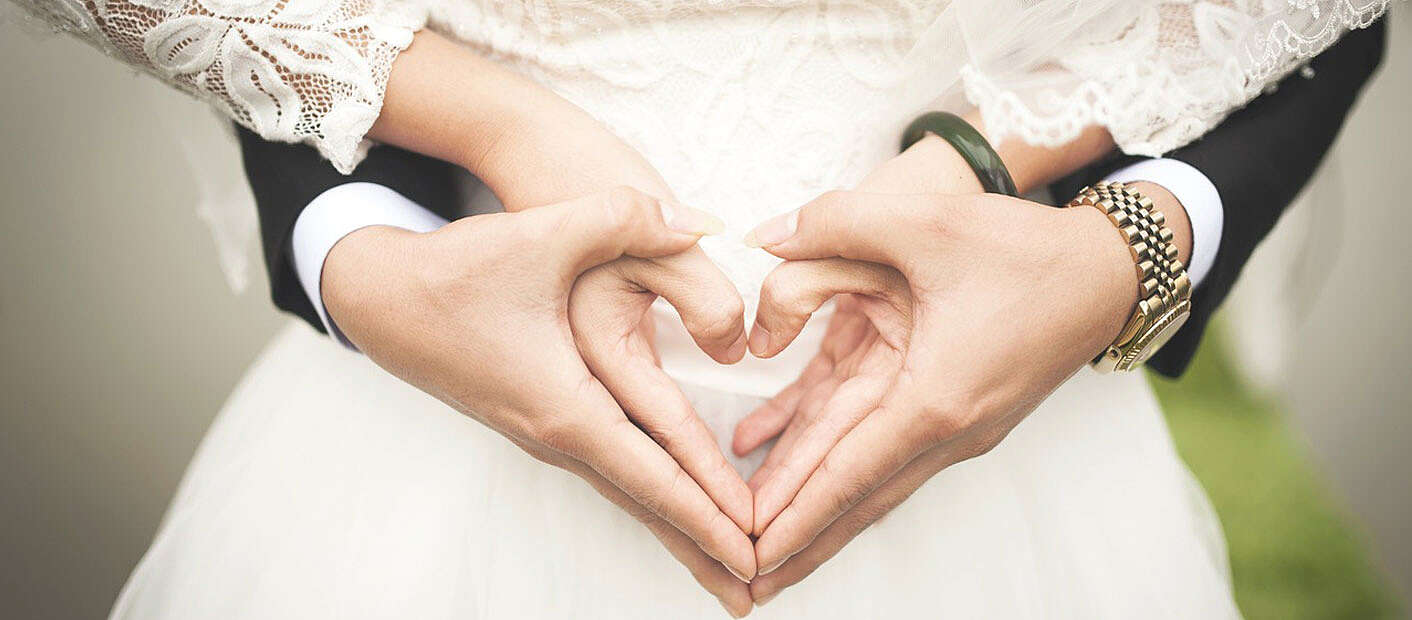 Hände eines Hochzeitspaares in Herzform verschlungen