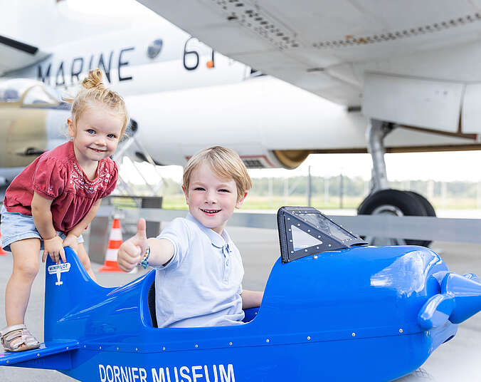 Kinder sitzen in einem Miniaturflugzeug.