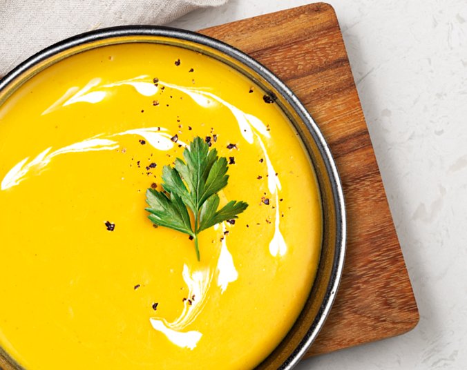 Kürbissuppe schön dekoriert in einer Schüssel auf einem Holzbrettchen.