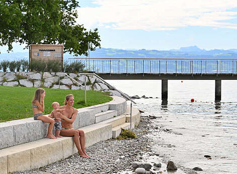 Mutter sitzt mit Mädchen und Baby auf Steinstufen am Bodenseeufer.