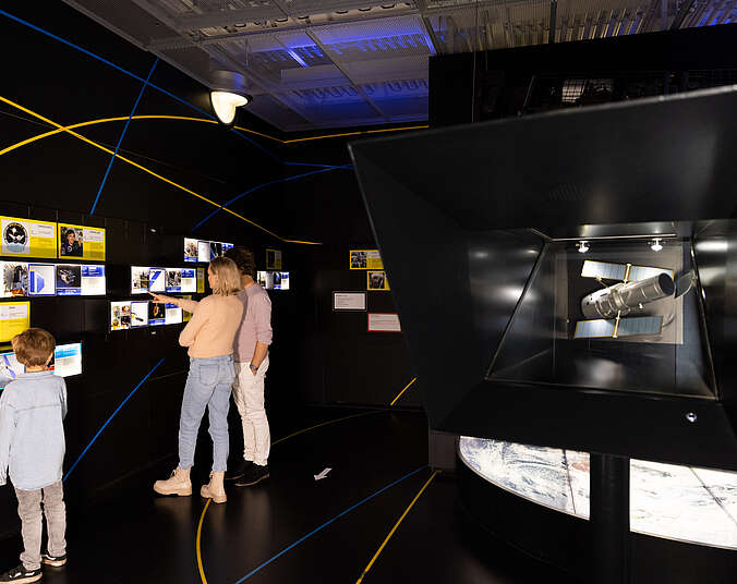 Eine Familie schaut in einem dunklen Raum eine Weltraumausstellung an.