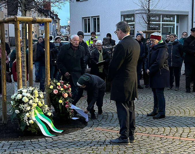 Männer und Frauen stehen vor Kränzen