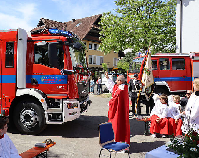 Pfarrer steht vor dem Feuerwehrfahrzeug und segnet es mit Weihwasser