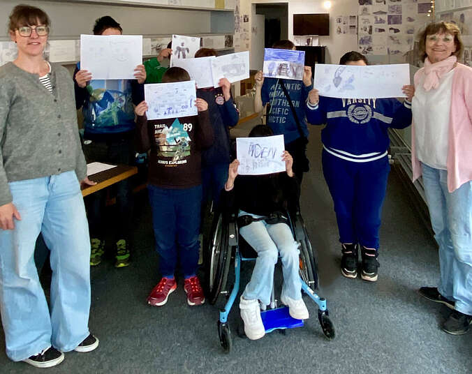 Jungen und Mädchen halten sich bemalte Blätter vor das Gesicht