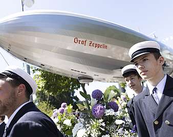 Festzug: Zeppelin-Modell begleitet von jungen Männern