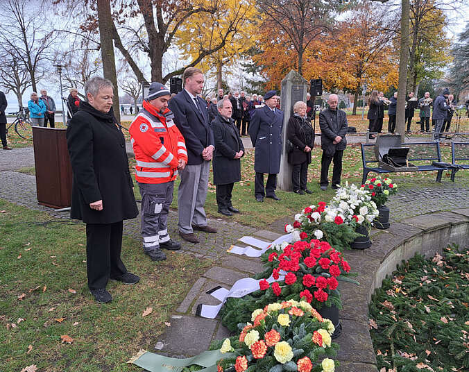 Männer und Frauen am Kriegerdenkmal, vor ihnen liegen Kränze