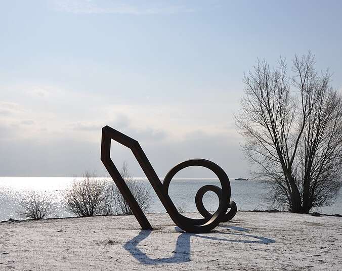 Blick auf eine Skulptur am Ufer des Bodensees im Winter - im Hintergrund der winterliche Bodensee.