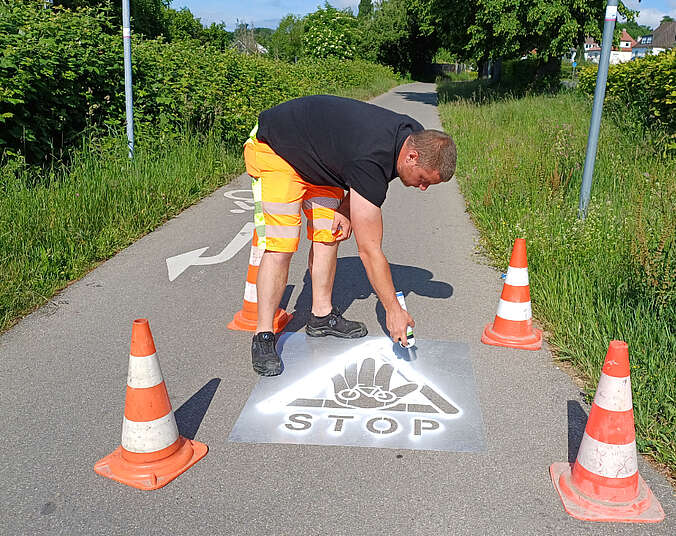 Mann sprüht Piktogramm auf die Straße, es zeigt eine Hand, ein Dreick und das Wort Stop
