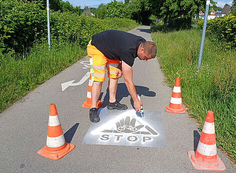 Mann sprüht Piktogramm auf die Straße, es zeigt eine Hand, ein Dreick und das Wort Stop
