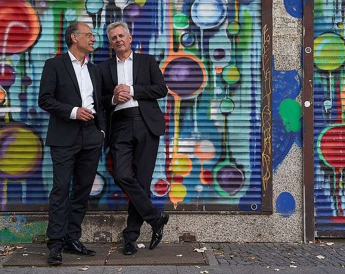 Zwei Männer lehnen an einer bunten Graffity-Wand