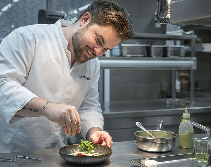 Koch steht in der Küche des Seegut Zeppelin und dekoriert einen Speiseteller.