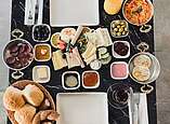 Frühstückstisch gedeckt mit Brötchen, Brotaufstrichen, Käse, Wurst, Oliven und Saft.