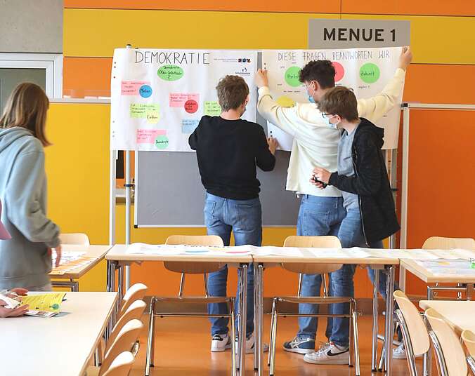 Drei Jugendliche hängen Plakate an Stellwand