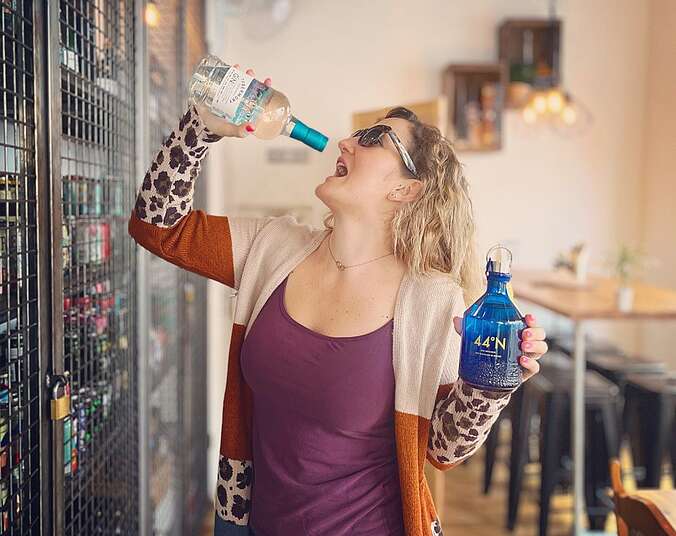 Eine Frau steht mit Sonnenbrille in der Minibar mit zwei Flaschen Gin.