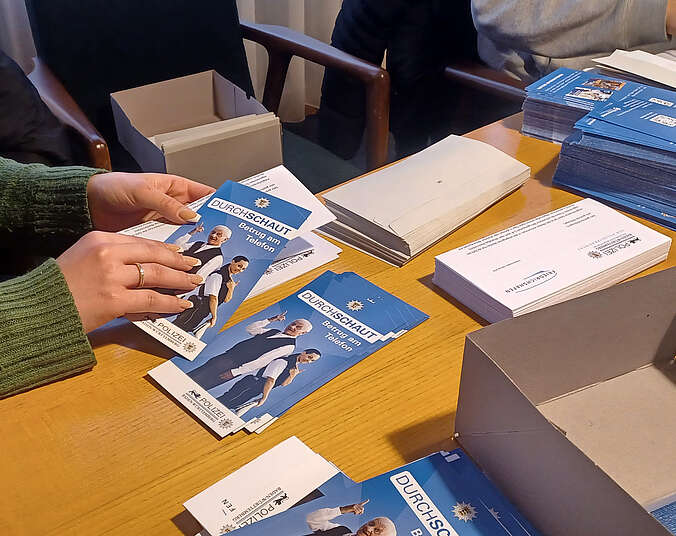 Hände, die Flyer und einen Brief in ein Kuvert stecken.