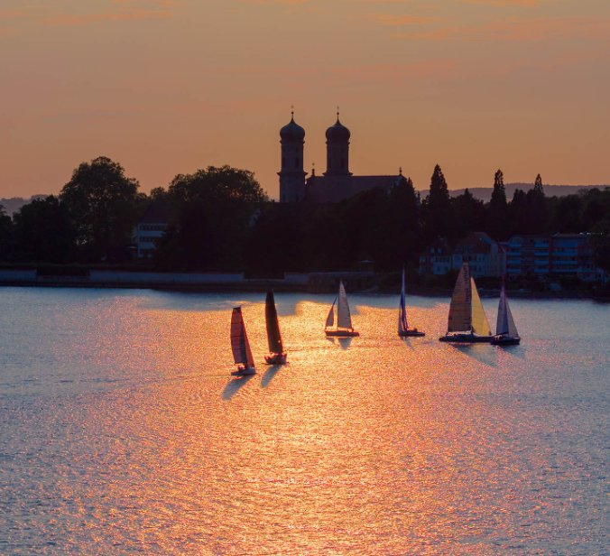 Bodensee mit Seegelbooten, Uferpark und Schlosskirche in der Abenddämmerung