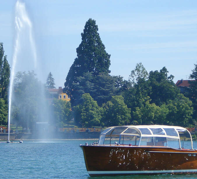 Holzschiff auf Bodensee vor Seefontäne und Ufer mit Bäumen