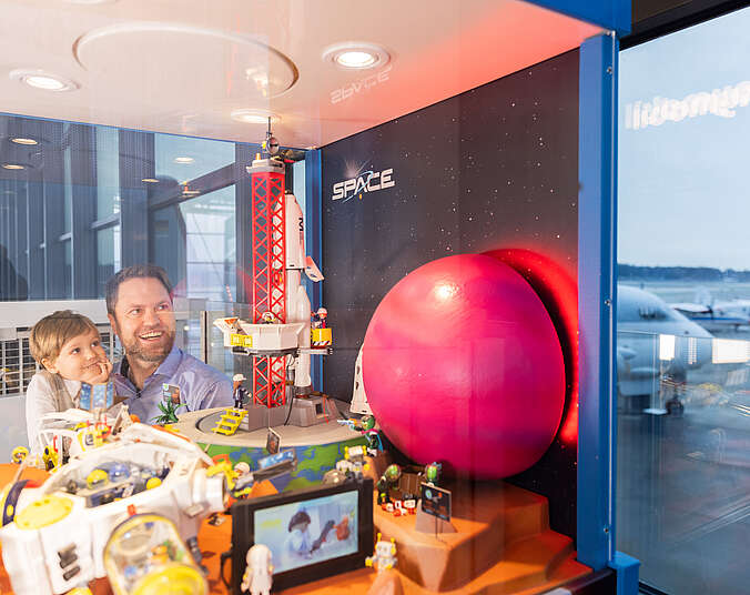 Mann und Junge schauen in ein Schaufenster mit raketenabschussrampe in Miniatur.