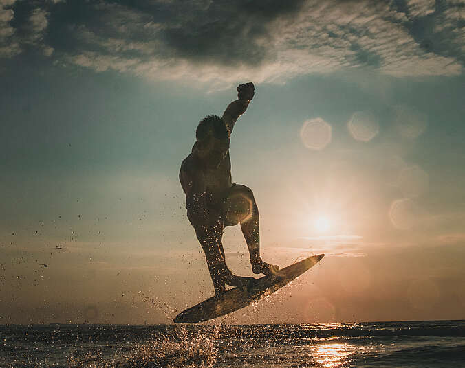 Person auf einem Skimboard vor Sonnenuntergang