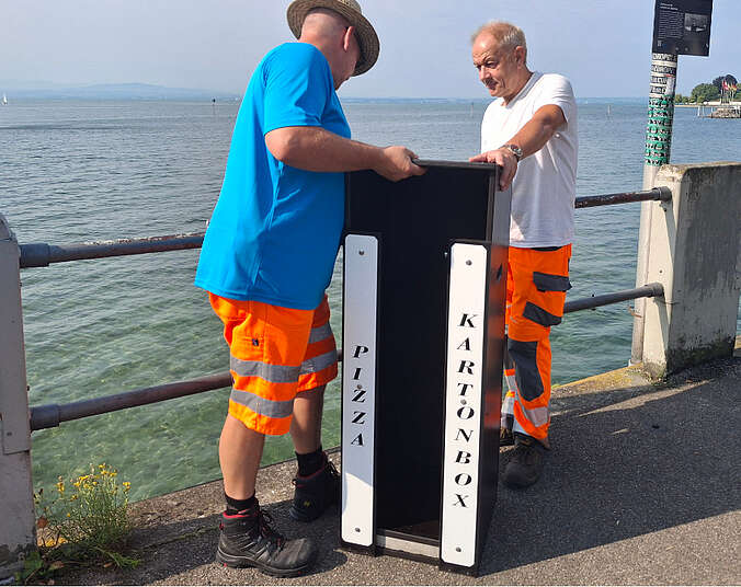 Zwei Männer stellen Box auf.