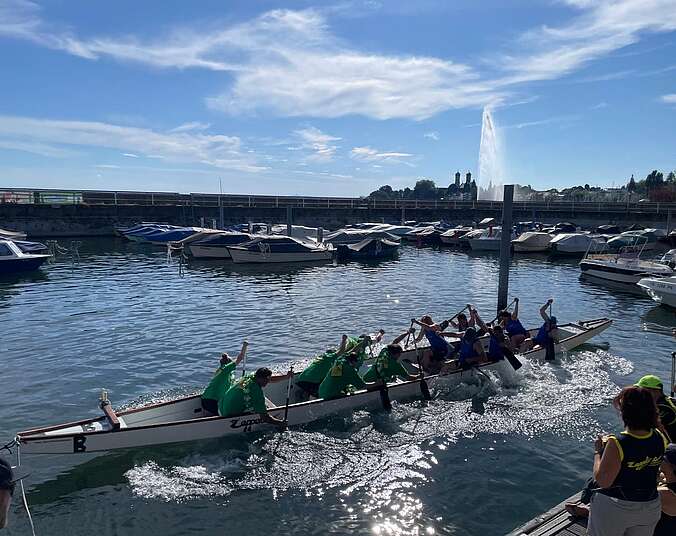 Drachenboot im Wasser mit zwei Teams und Publikum am Hafen
