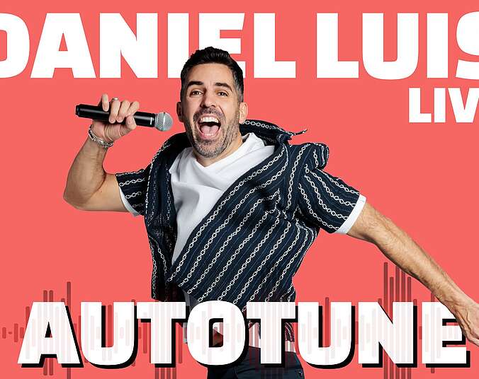 Ein lachender Mann mit Drei-Tage-Bart lacht in die Kamera und hält ein Mikrofon vor seine Mund.