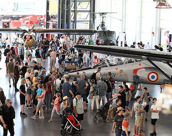 Frauen, Männer und Kinder, die im Hangar des Dornier Museum die historischen Flugzeuge beim Sommerfest besichtigen.