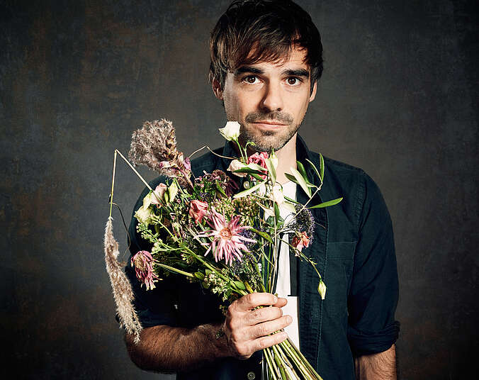 Sebastian Lehmann mit Blumenstrauß in der Hand vor dunklem Hintergrund
