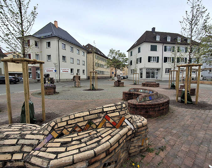 Platz mit Mahnmal aus glasiertem Backstein mit Bäumen dazwischen