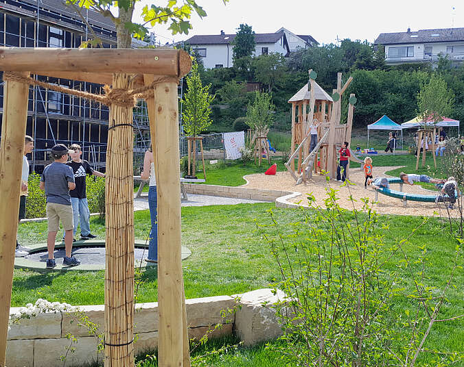 Grüne Wiese, Kinder, Spielgeräte. Im Hintergrund ein Kletterturm aus Holz.