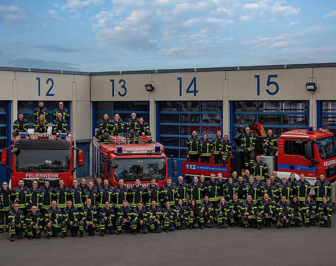 Männer und Frauen der Feuerwehr, im Hintergrund Feuerwehrfahrzeuge