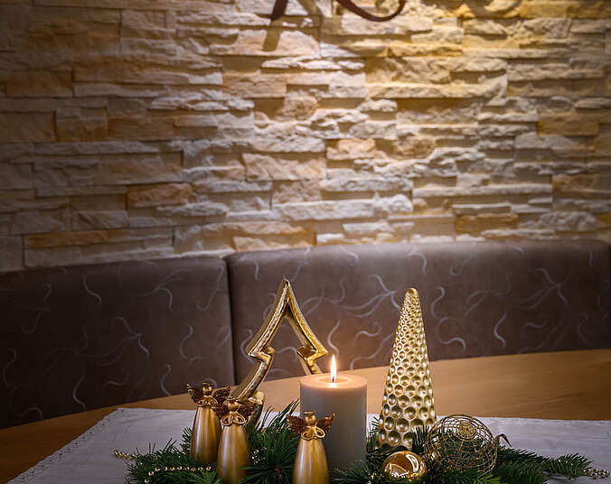 Auf einem Tisch steht ein Adventsgesteck mit einer brennenden Kerze.