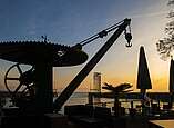 Ehemaliger Salzkran am Hafen von Friedrichshafen mit zugeklappten Sonnenschirmen und Sonnenuntergang im Hintergrund.