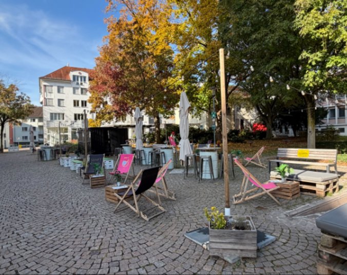Container-Bar mit Liegestühlen und Tischen auf gepflastertem Platz