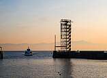 Hafeneinfahrt im Sonnenuntergang mit Blick auf den Moleturm in Friedrichshafen und ein einfahrendes Schiff.