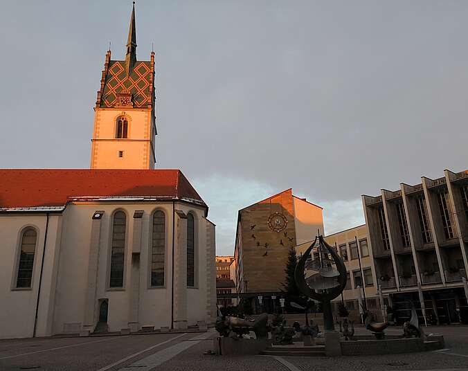 Man sieht die Nikolauskirche auf dem Adenauerplatz, beleuchtet von der Abendsonne