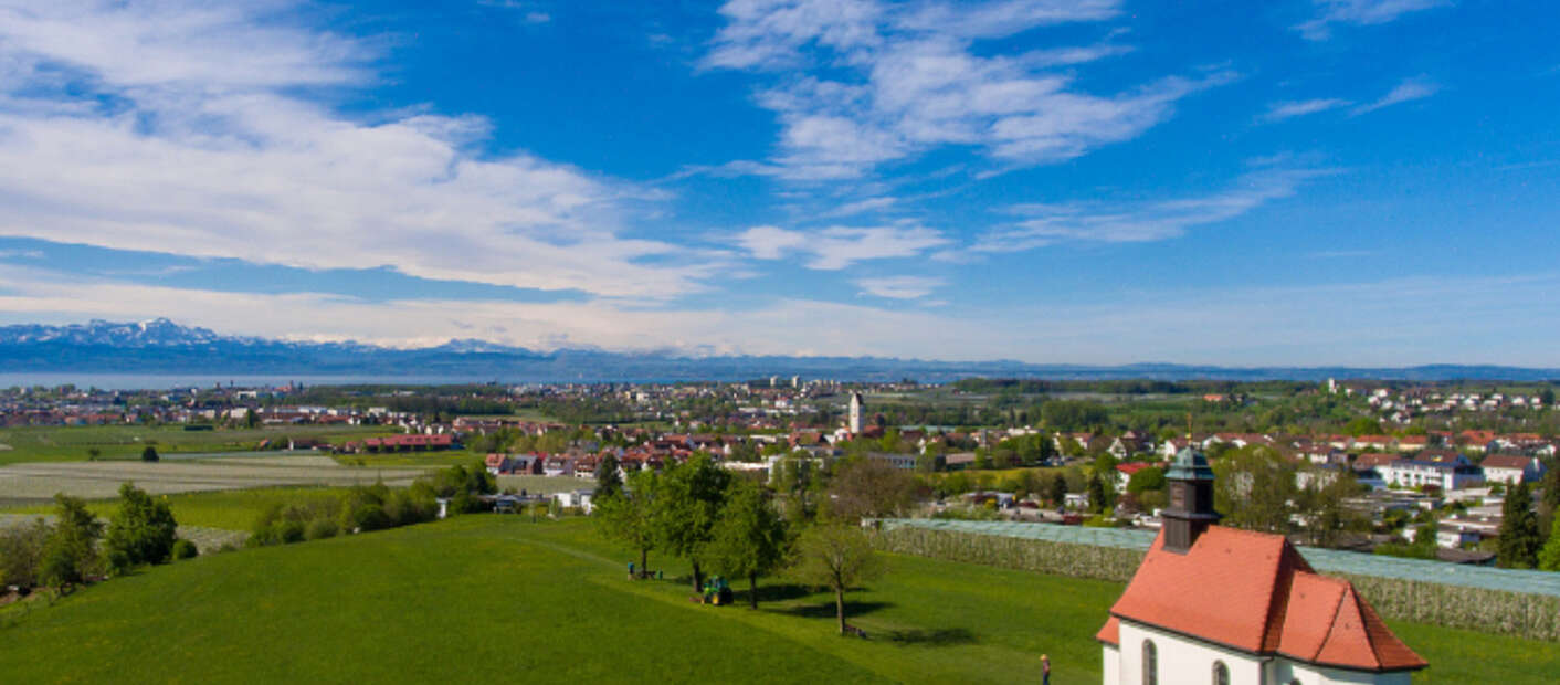 Lufbild: Haldenbergkapelle inmitten grüner Wiese, im Hintergrund Bodenseepanorama mit Alpen