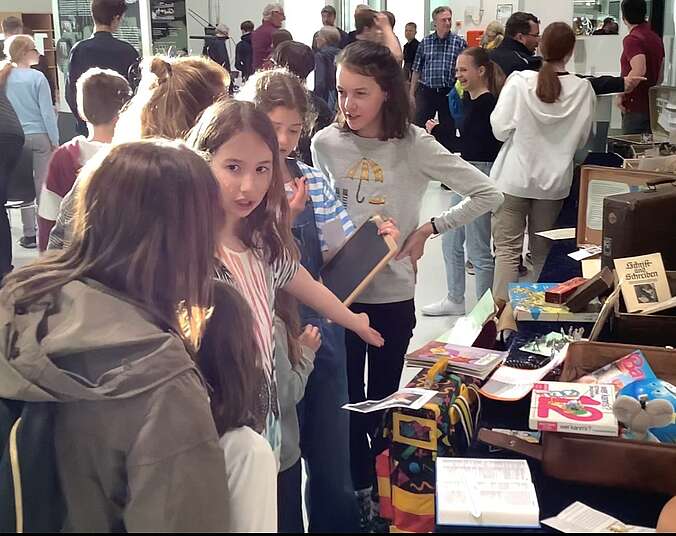 Schülerinnen erklären ihre Koffer-Ausstellung über Kindheiten.