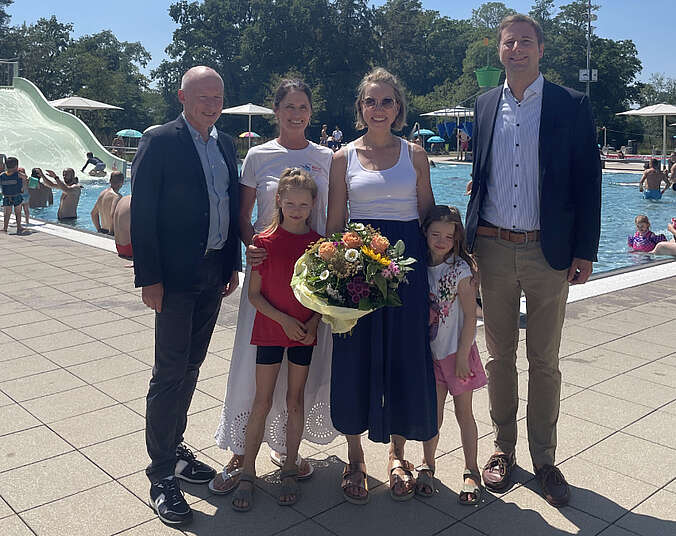 Gruppenbild: Mutter und Töchter bekommen Blumenstrauß und Gutschein vor Schwimmbecken überreicht.