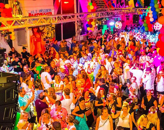 Frauen und Männer tanzen auf einem dekoriertem Partyboot.