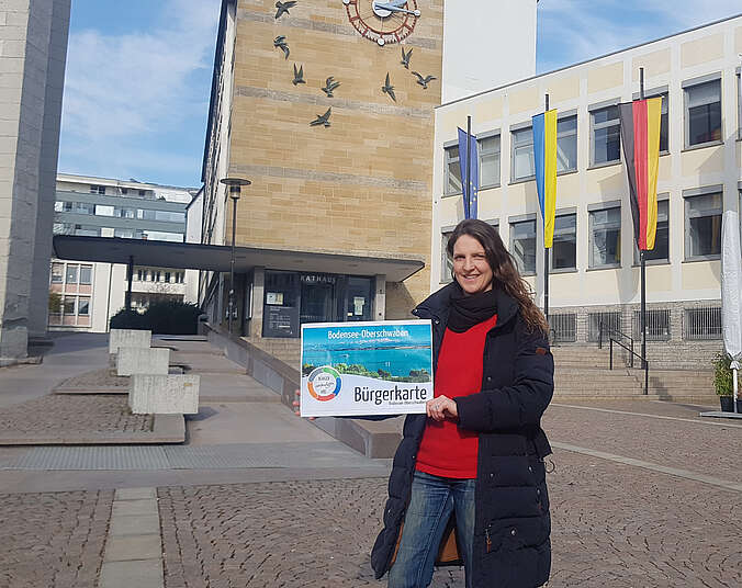 Frau präsentiert Bürgerkarte vor dem Rathaus.